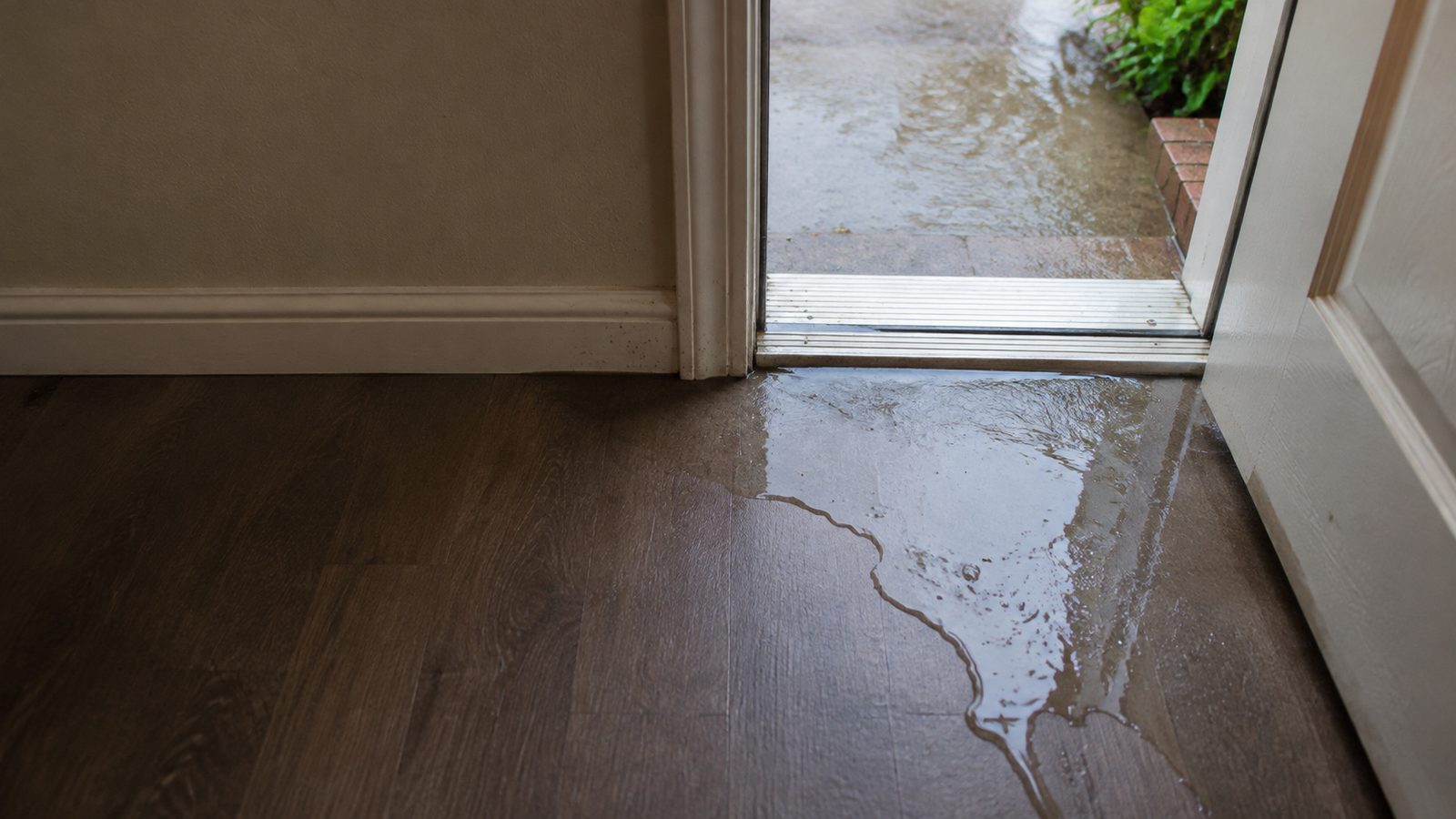 Shallow rainwater crossing an exterior doorway threshold onto an interior floor